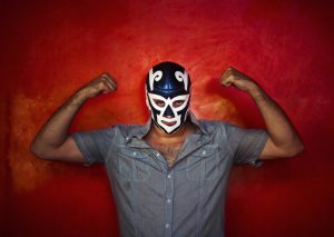 mexican luchador with a blue mask showing off in front of a red wall